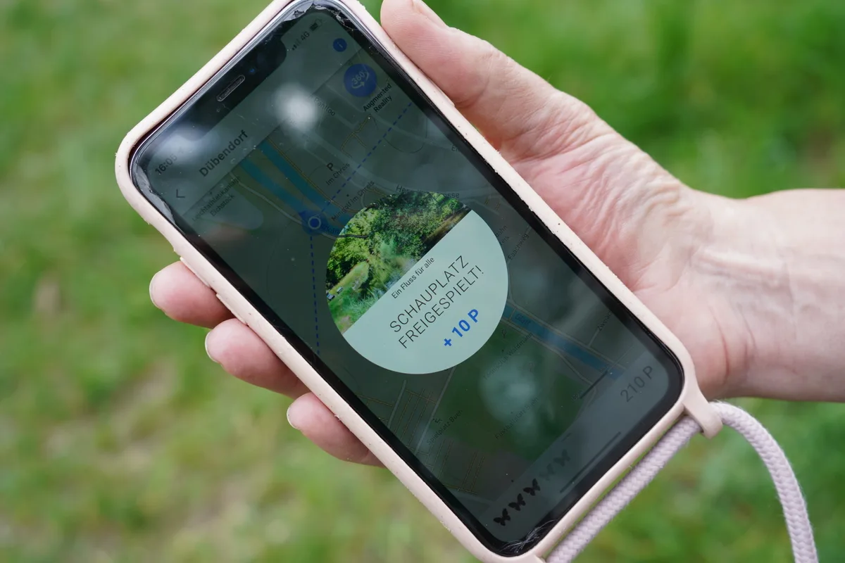 Eine Hand, die ein Smartphone hält. Auf dem Display steht: «Schauplatz freigespielt!».